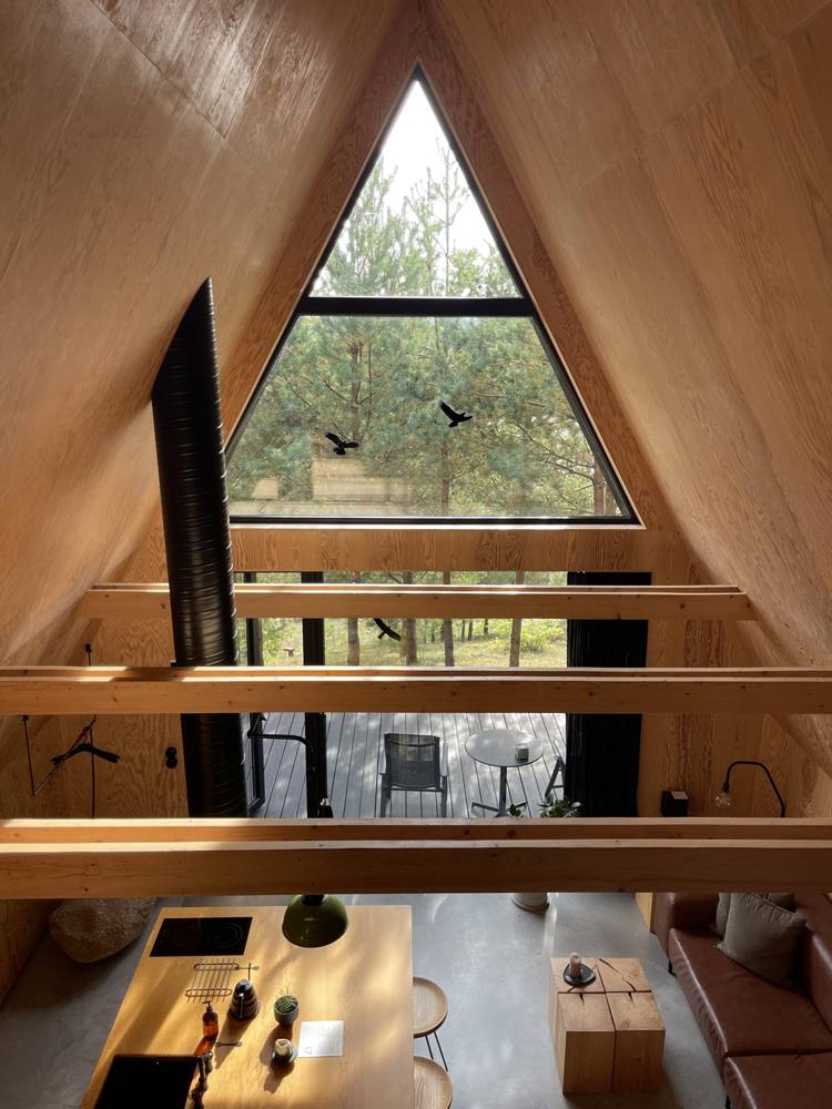 View from the mezzanine of an A-frame cabin at DOYOU PLACE, Lithuania, looking down and out through the triangular window