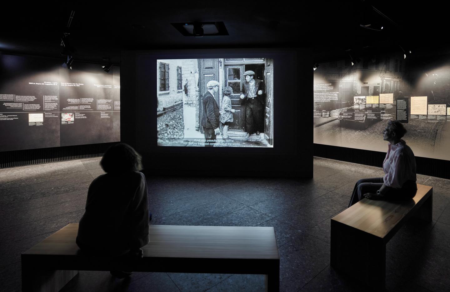 Visitors on benches watching archival film footage