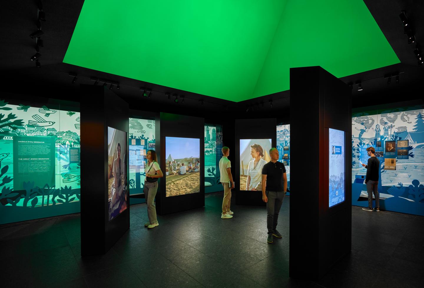 Visitors in the Dreams and Reality Gallery among tall screens showing young people of the shtetl