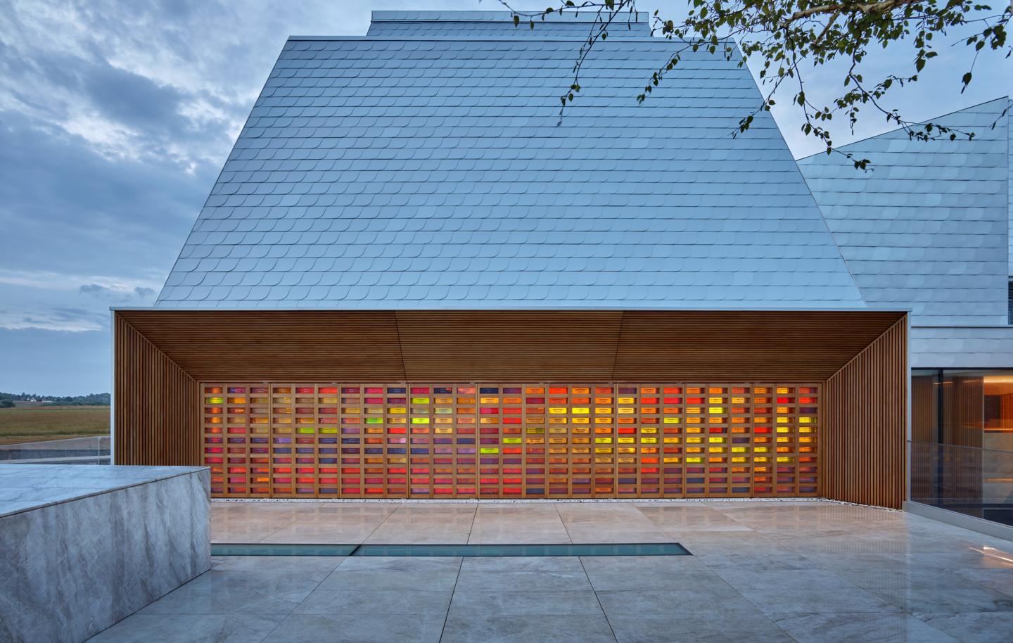 The memorial wall of coloured glass under the museum's wooden canopy at dusk