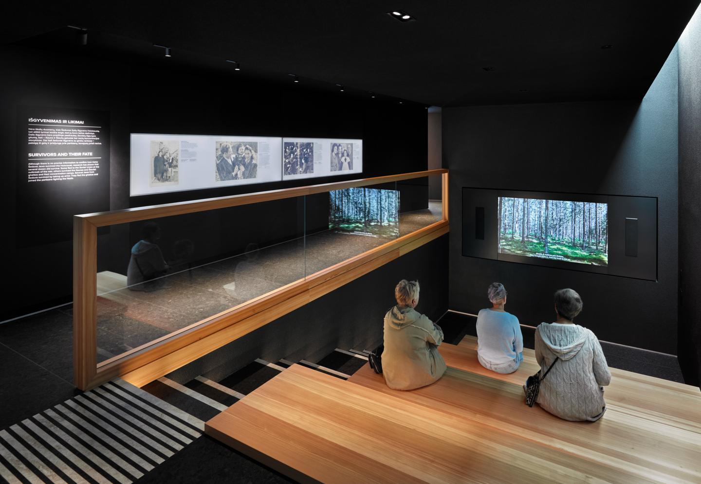 Visitors seated on wooden steps in the Survivors and Their Fate section