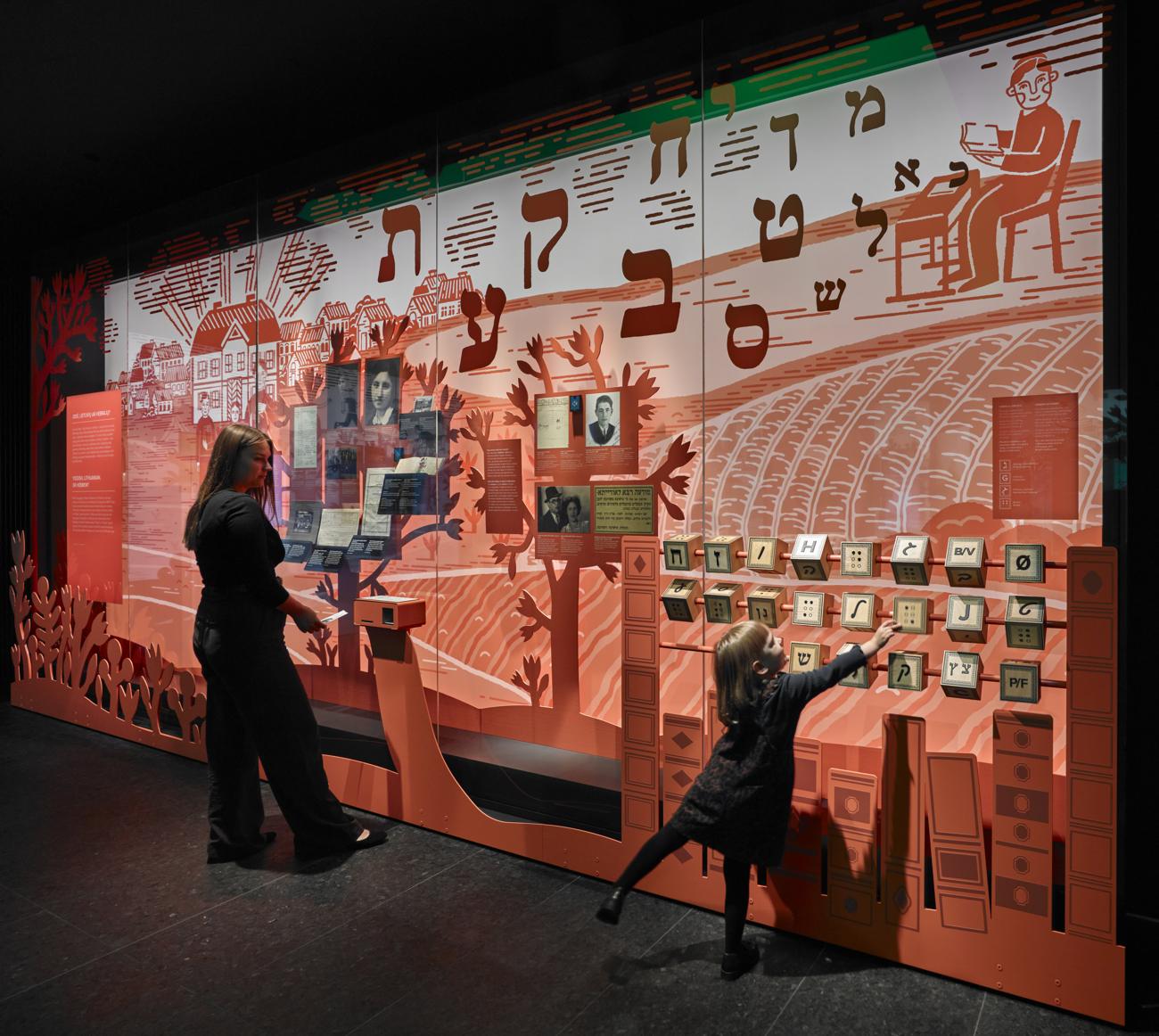 A child plays with Hebrew letter blocks at an illustrated wall about Yiddish, Lithuanian and Hebrew
