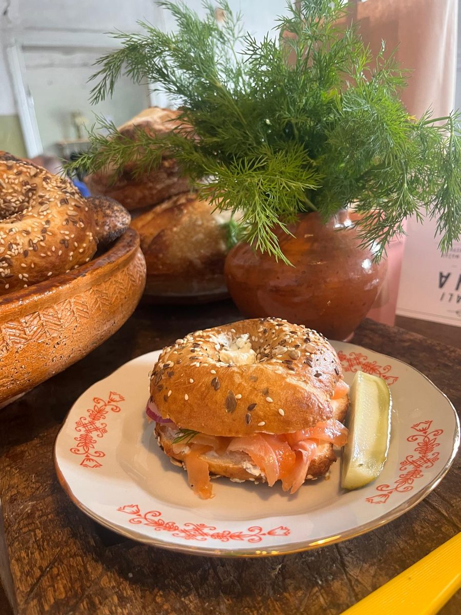 A bagel with smoked salmon and a pickle on a decorative plate, dill in the background