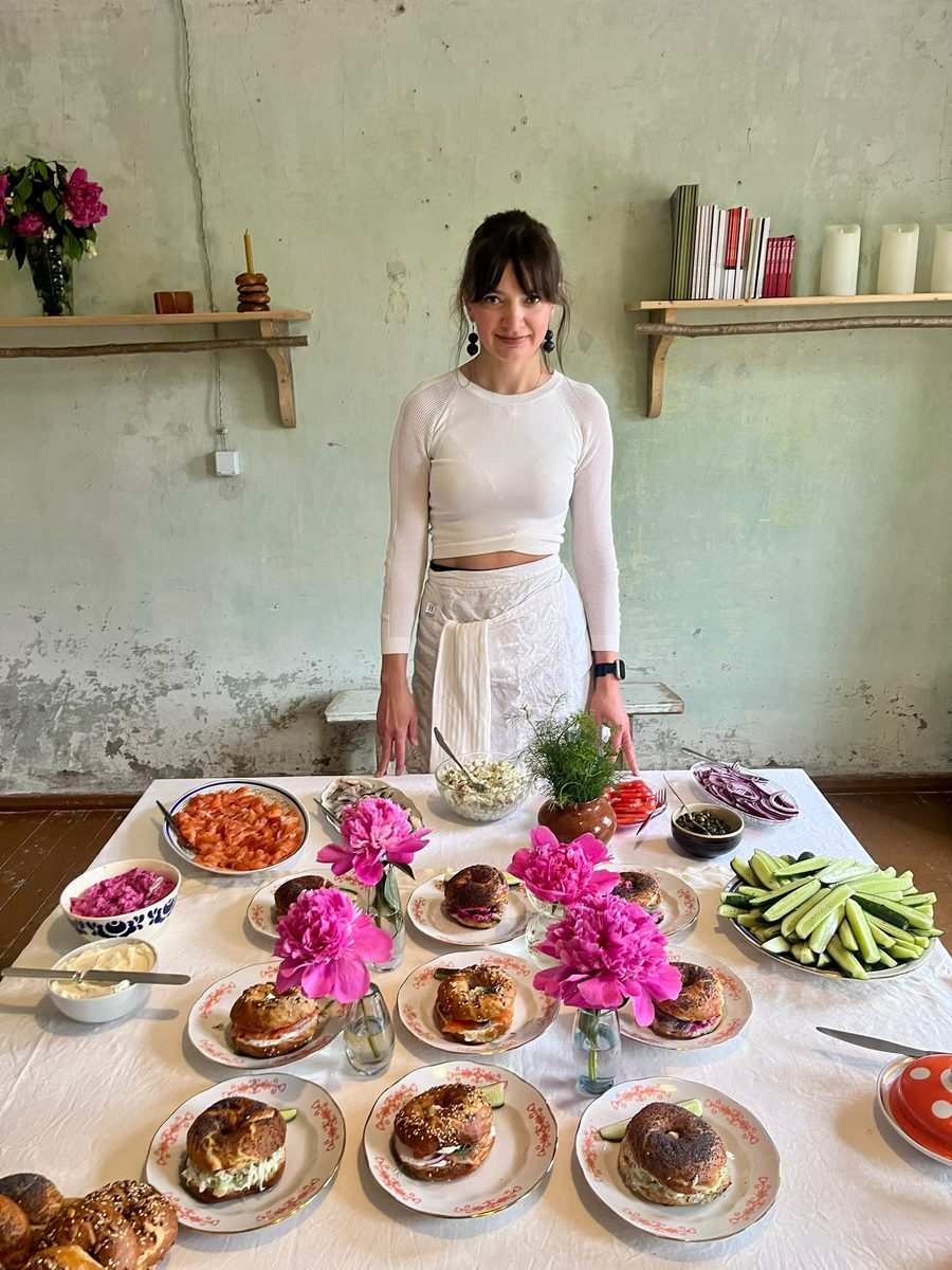 Ernesta standing behind a table of bagels, flowers and salads in the old house in Žagarė