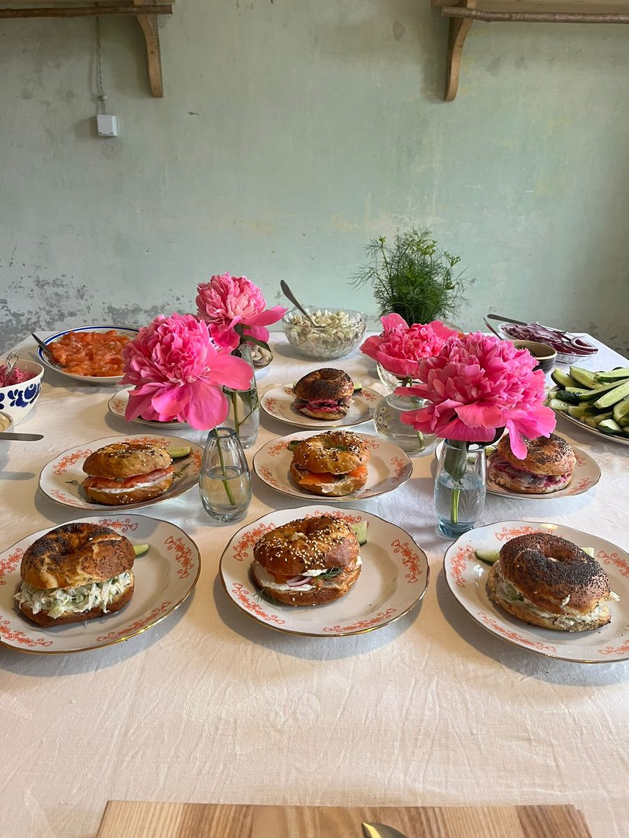 A table laid with plates of bagels, pink peonies and fresh dill